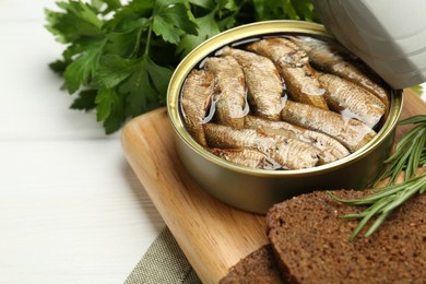 Photo of Canned sprats, herbs and bread on white wooden table, closeup. Space for text