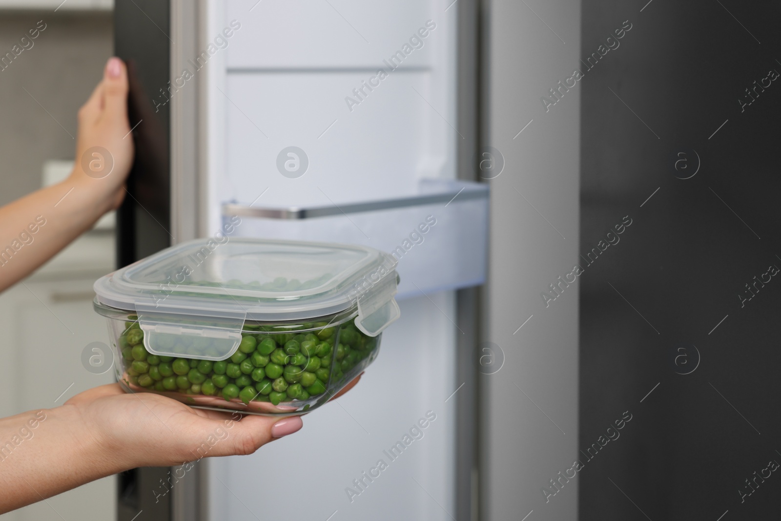 Photo of Woman putting container with tasty peas into fridge, closeup and space for text. Food storage