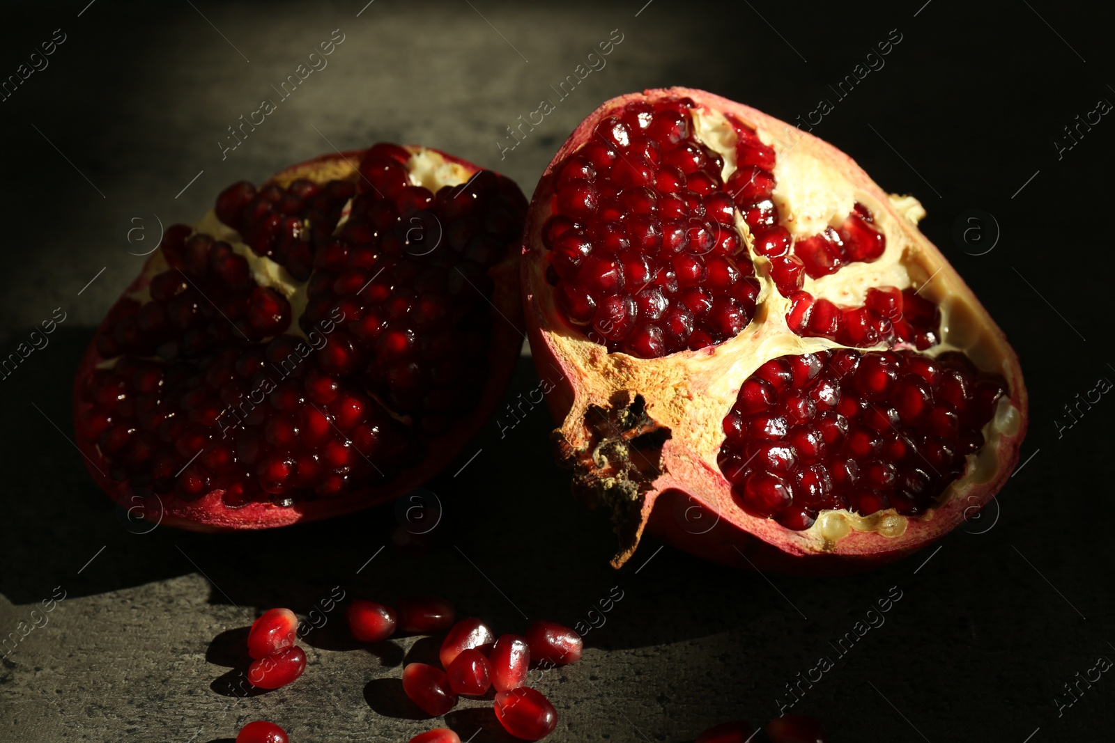 Photo of Pieces of ripe juicy red pomegranate with grains on grey textured table, closeup