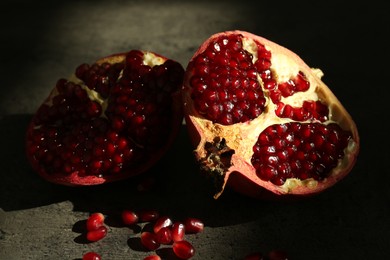 Photo of Pieces of ripe juicy red pomegranate with grains on grey textured table, closeup