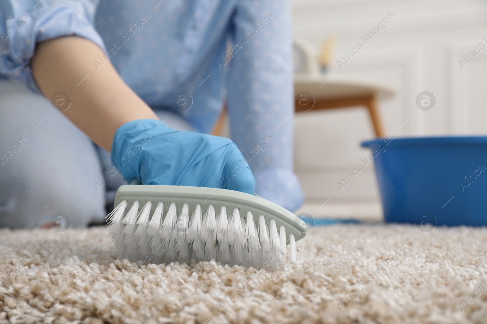 Photo of Woman in rubber gloves cleaning carpet with brush indoors, closeup. Space for text