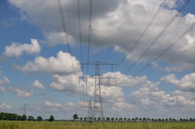 Modern high voltage towers in field on sunny day