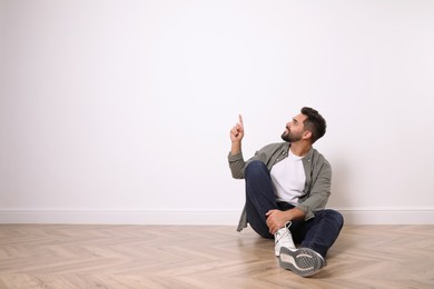 Photo of Young man sitting on floor near white wall indoors. Space for text