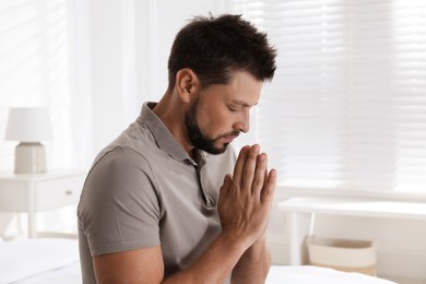 Photo of Religious man with clasped hands praying at home
