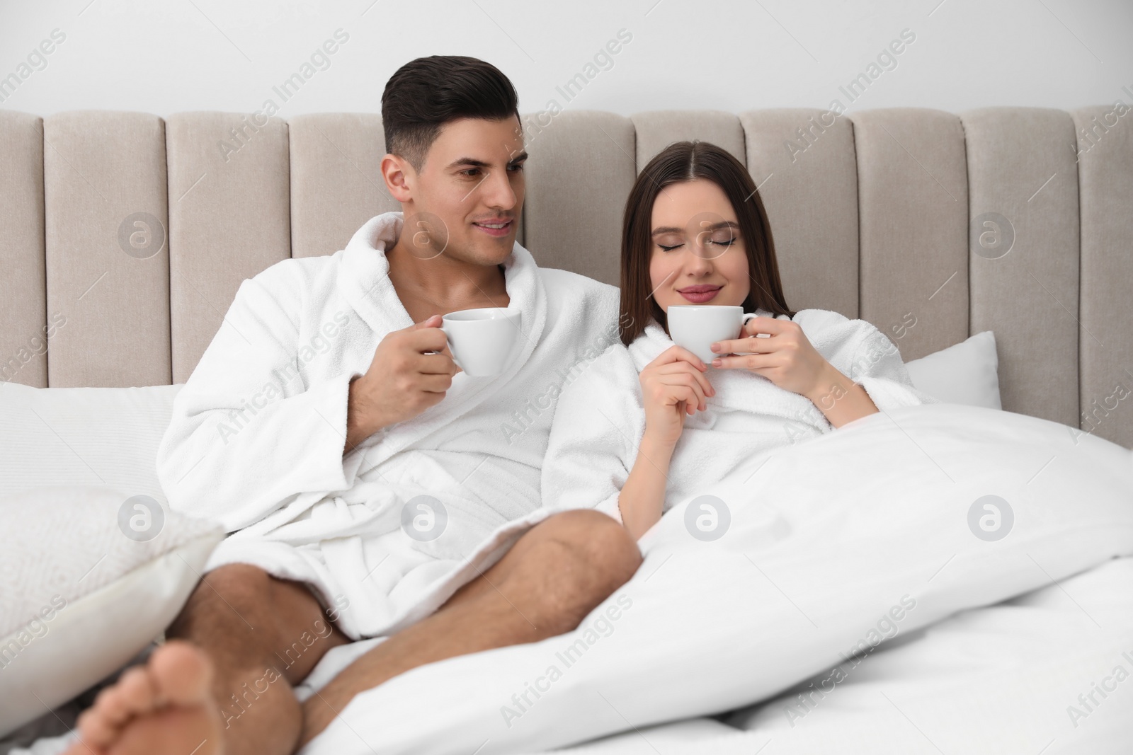 Photo of Happy couple in bathrobes with coffee on bed at home