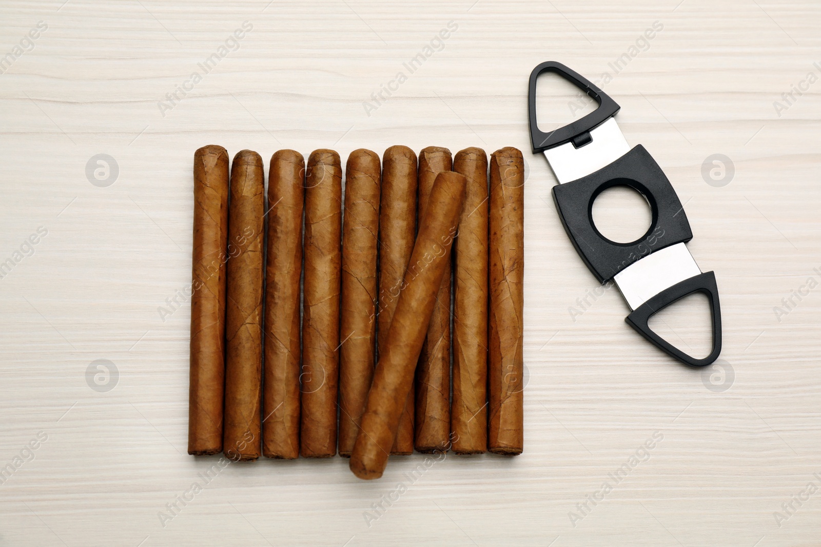 Photo of Cigars and guillotine cutter on white wooden table, flat lay