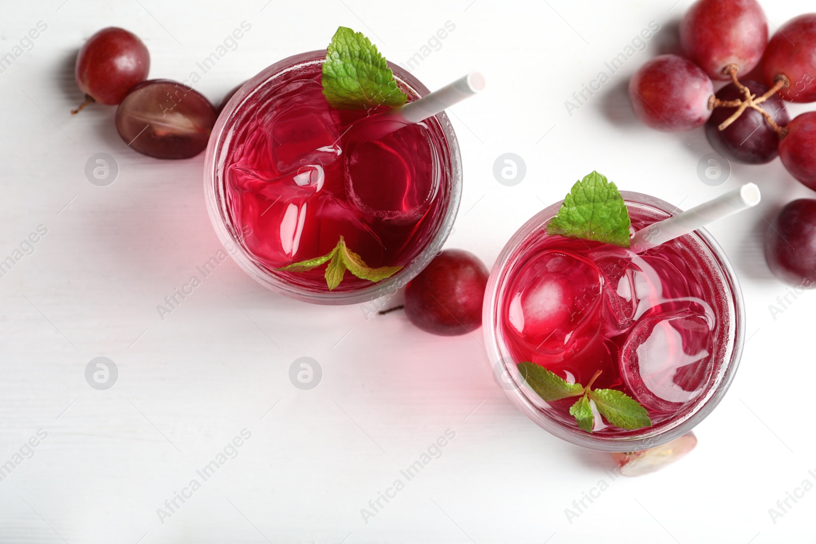 Photo of Delicious grape soda water and berries on white wooden table, flat lay. Refreshing drink