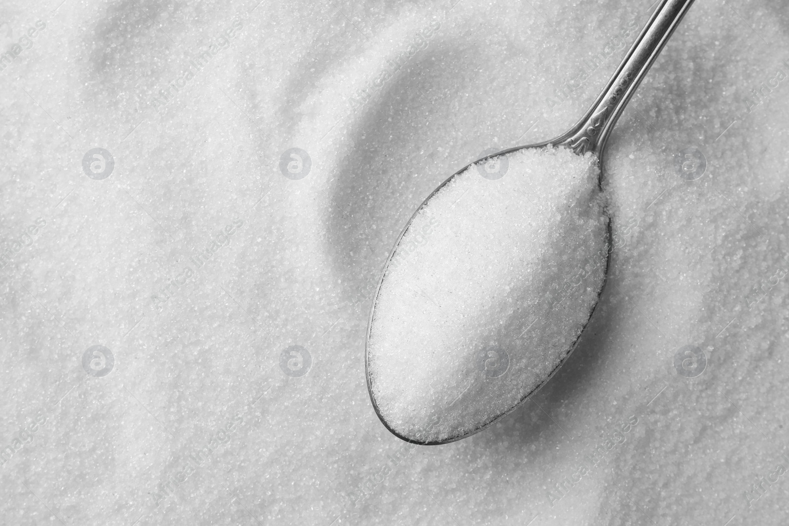 Photo of Metal spoon on granulated sugar, top view