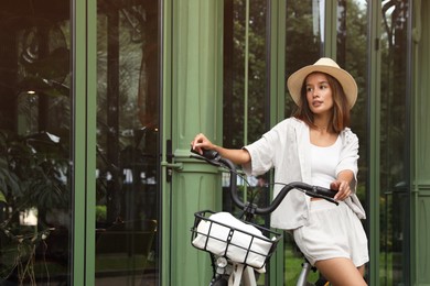 Photo of Beautiful young woman with bicycle near modern building outdoors. Space for text
