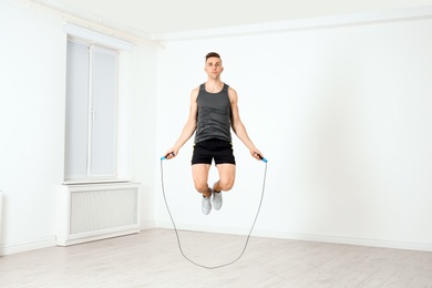 Full length portrait of young sportive man training with jump rope in light room