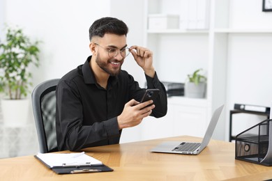 Photo of Handsome young man using smartphone at wooden table in office