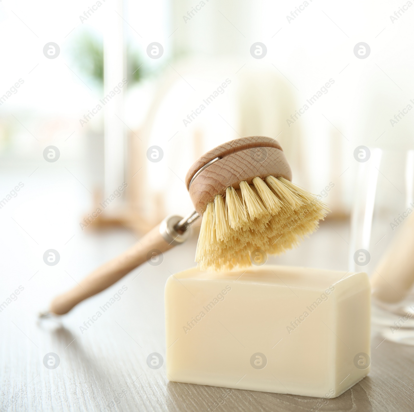 Photo of Cleaning brush and soap bar for dish washing on wooden table, closeup