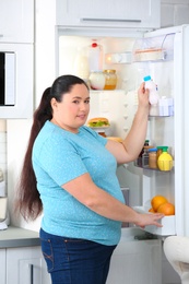 Overweight woman taking yogurt from refrigerator in kitchen. Healthy diet