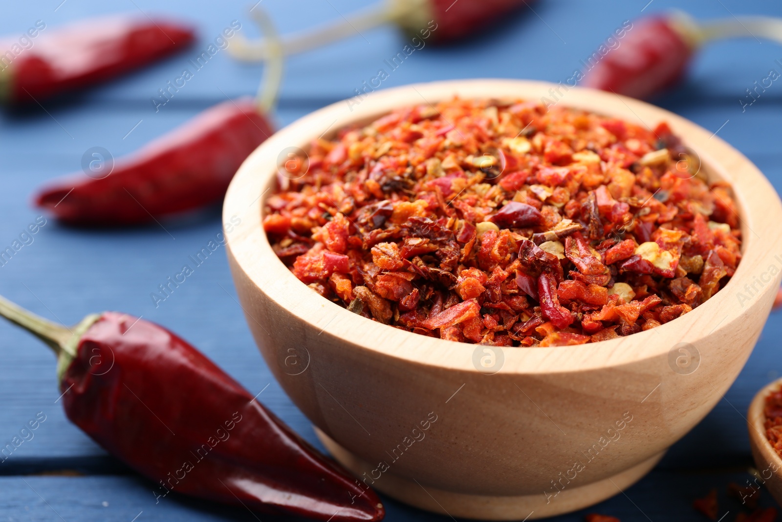 Photo of Chili pepper flakes in bowl and pods on blue wooden table, closeup