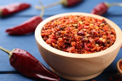 Chili pepper flakes in bowl and pods on blue wooden table, closeup