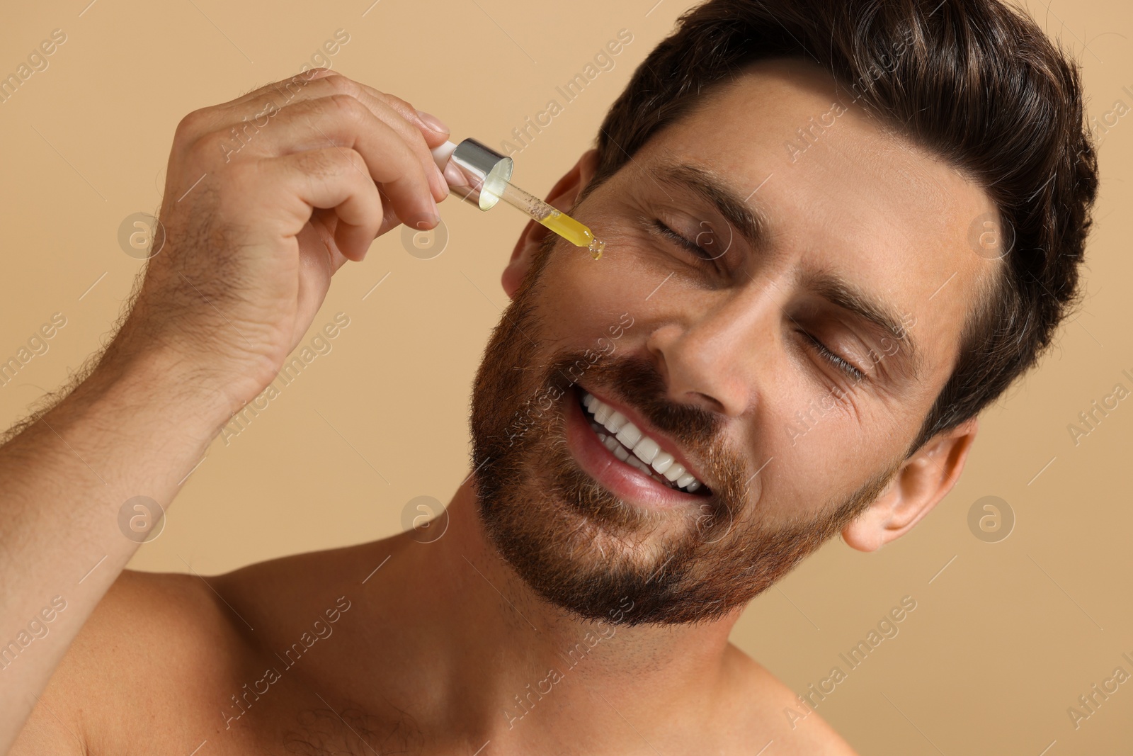 Photo of Smiling man applying cosmetic serum onto his face on beige background, closeup