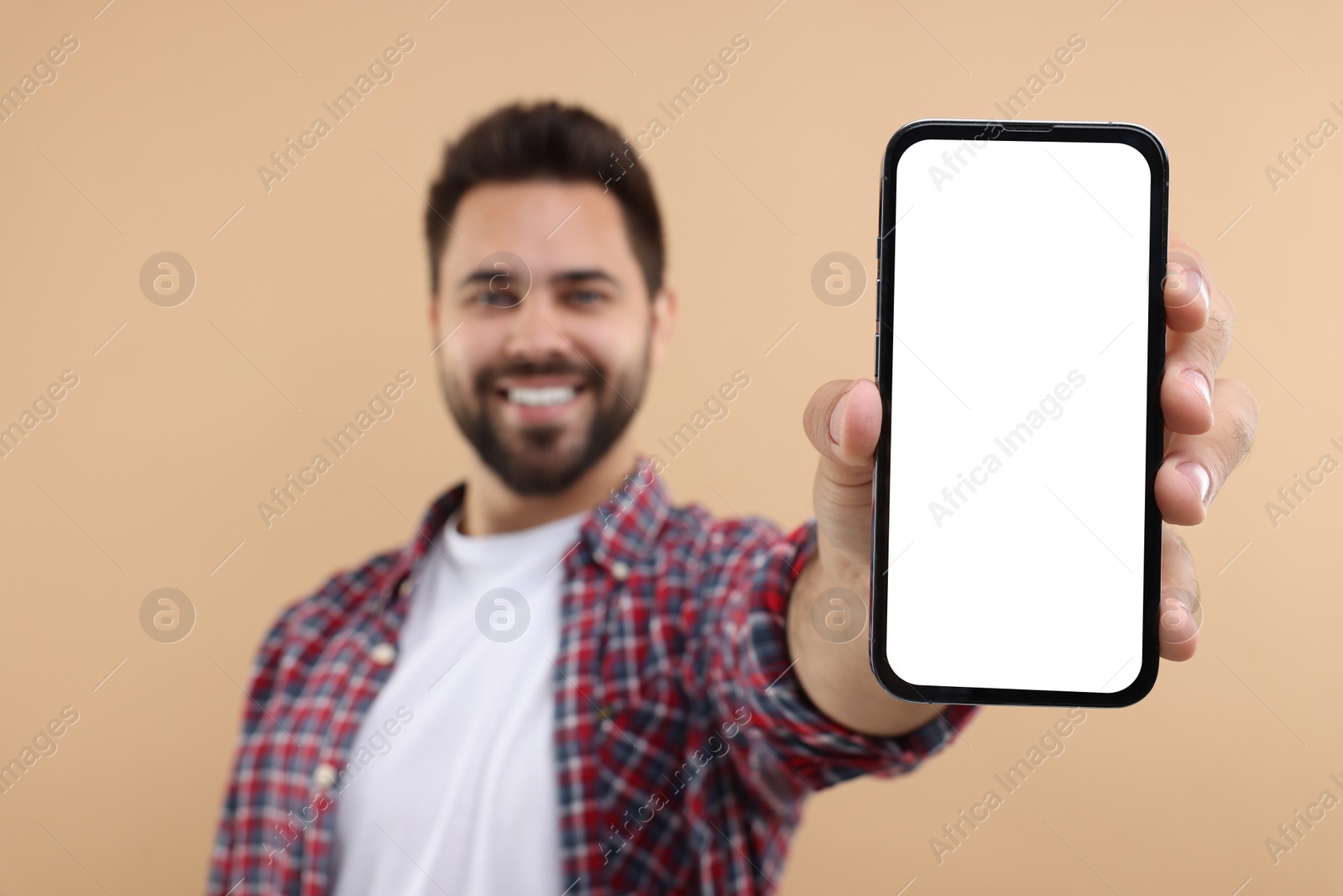 Photo of Young man showing smartphone in hand on beige background, selective focus. Mockup for design