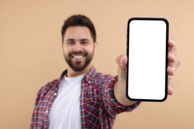 Young man showing smartphone in hand on beige background, selective focus. Mockup for design