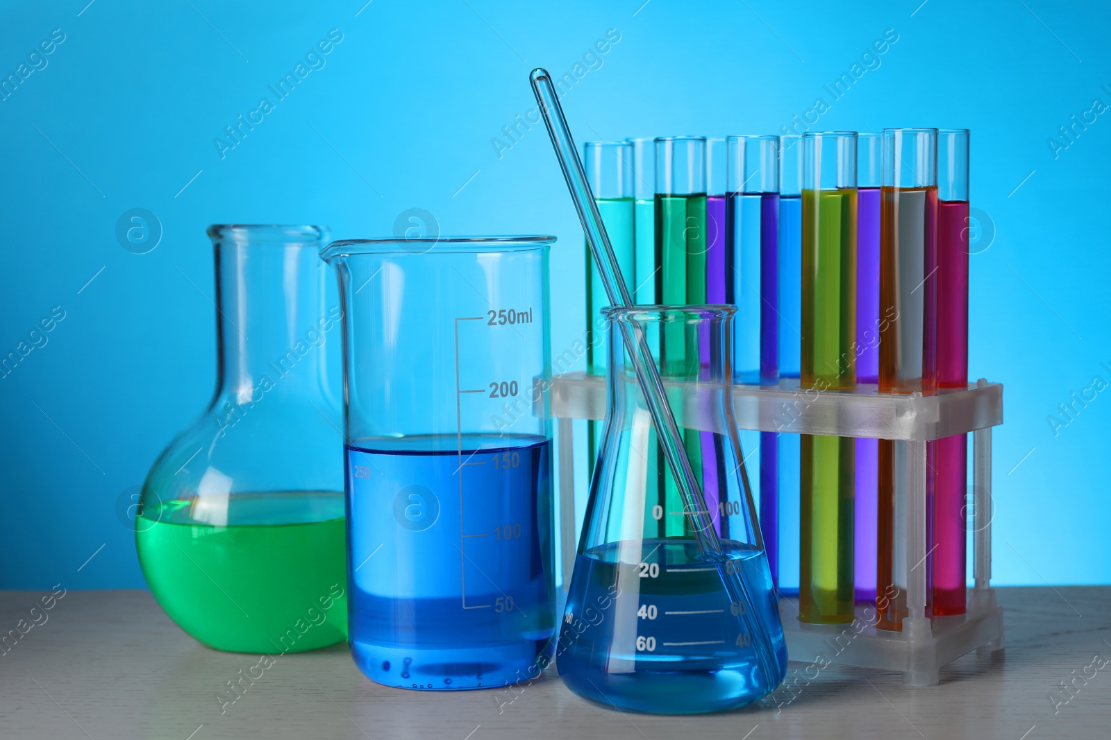 Photo of Different laboratory glassware with colorful liquids on wooden table against light blue background