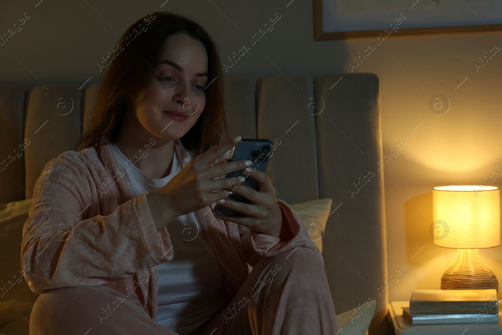 Photo of Woman using smartphone in bedroom at night. Internet addiction