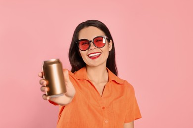 Beautiful young woman holding tin can with beverage on pink background