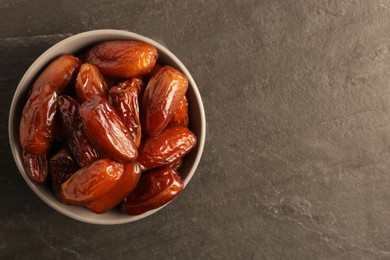 Tasty sweet dried dates in bowl on black table, top view. Space for text