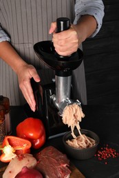 Photo of Woman making chicken mince with electric meat grinder at black table, closeup