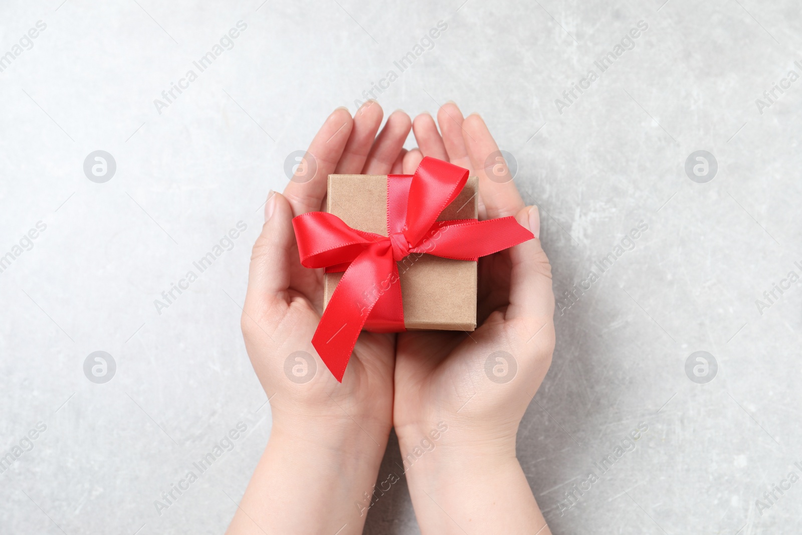 Photo of Woman holding gift box with red bow at light grey table, top view