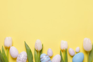 Photo of Flat lay composition of painted Easter eggs and tulip flowers on yellow background. Space for text