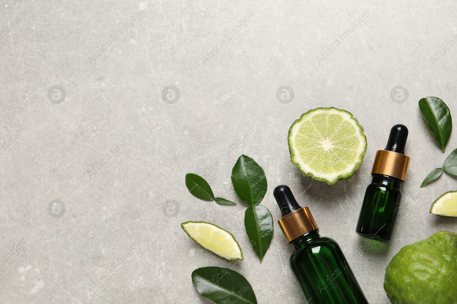 Photo of Glass bottles of bergamot essential oil and fresh fruits on light table, flat lay. Space for text