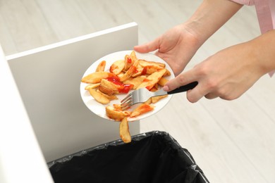 Woman throwing baked potato with ketchup into bin indoors, closeup