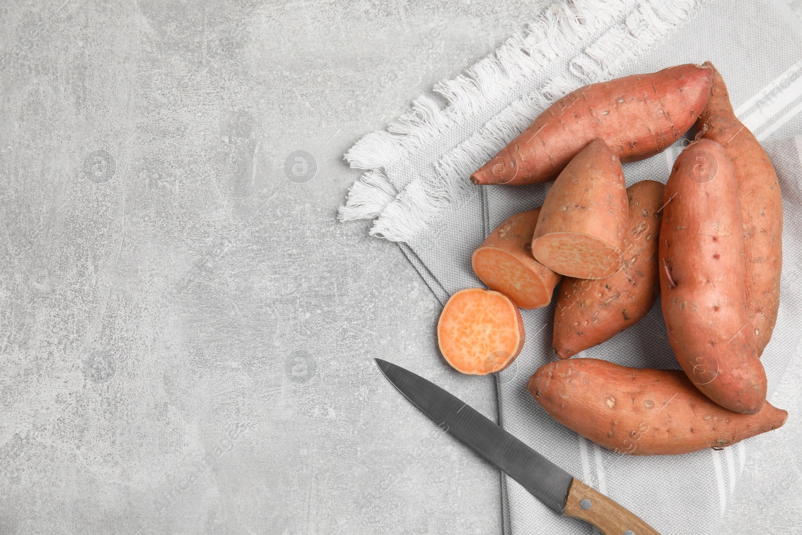 Photo of Whole and cut ripe sweet potatoes on grey table, top view. Space for text