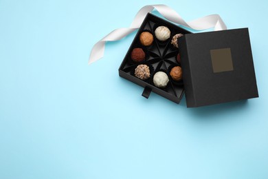 Box of tasty chocolate candies and ribbon on light blue background, flat lay. Space for text