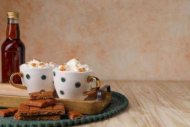 Delicious coffee with whipped cream and caramel syrup on wooden table, space for text