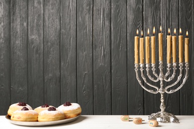 Photo of Silver menorah near sufganiyot and dreidels with symbols Nun, He, Pe, Gimel on grey wooden background. Space for text