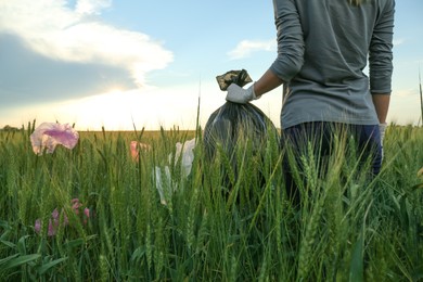 Photo of Woman with trash bag collecting garbage in wheat field, closeup