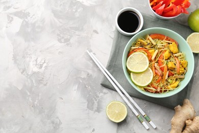 Photo of Stir-fry. Delicious cooked noodles with chicken and vegetables in bowl served on gray textured table, flat lay. Space for text