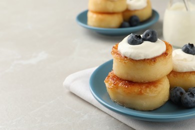 Photo of Delicious cottage cheese pancakes with blueberries, honey and sour cream on light table, closeup. Space for text