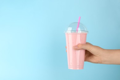 Photo of Woman with plastic cup of tasty smoothie on light blue background, closeup. Space for text