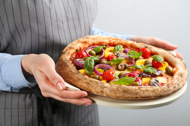 Woman holding tasty vegetable pizza on light grey background, closeup