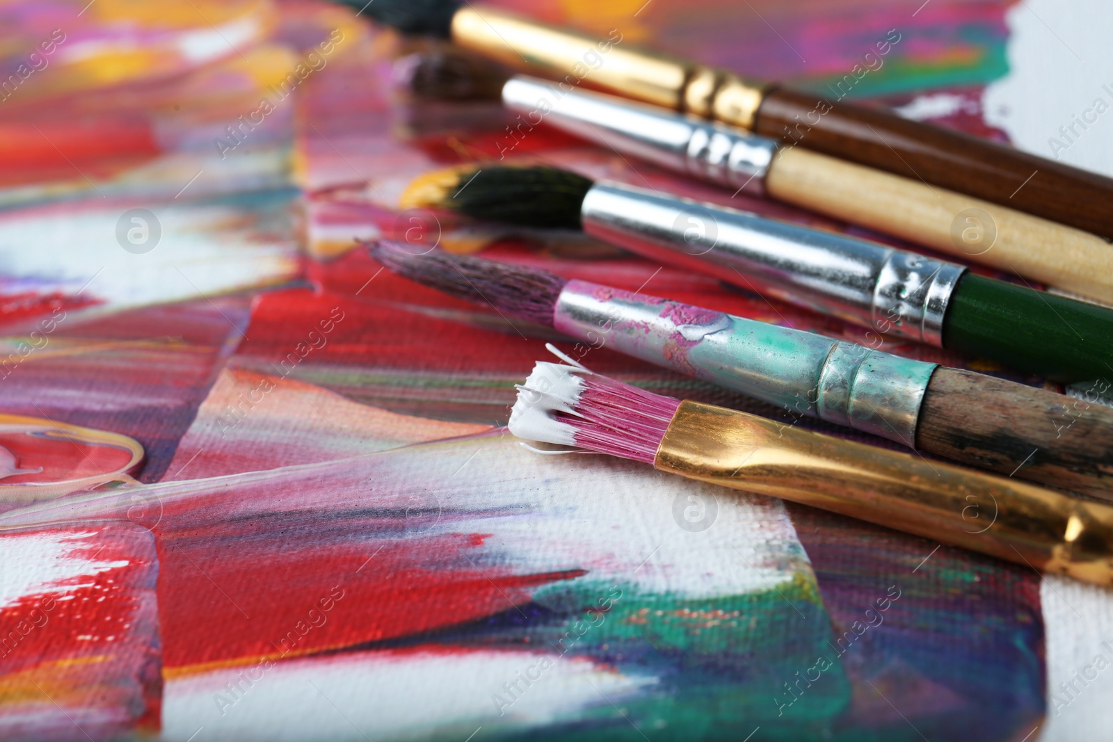 Photo of Set of different brushes on abstract colorful paint, closeup