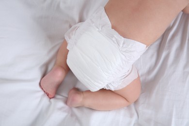 Top view of cute baby in dry soft diaper on white bed