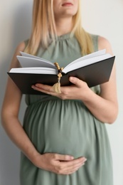 Young pregnant woman with Bible praying on light background