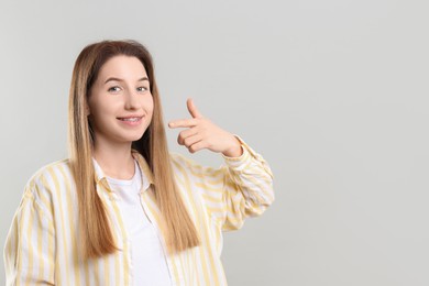 Portrait of smiling woman pointing at her dental braces on grey background. Space for text