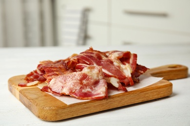 Slices of tasty fried bacon on white wooden table indoors