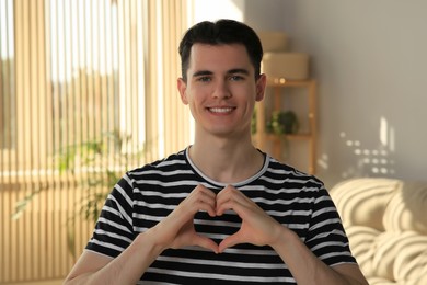 Photo of Happy volunteer making heart with his hands in room