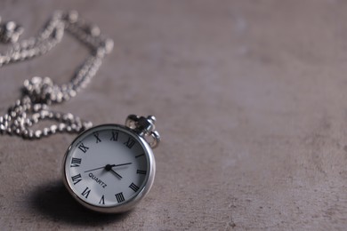 Silver pocket clock with chain on grey textured table, closeup. Space for text