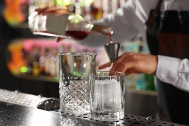Photo of Cocktail making. Bartender pouring alcohol from bottle into jigger at counter in bar, selective focus
