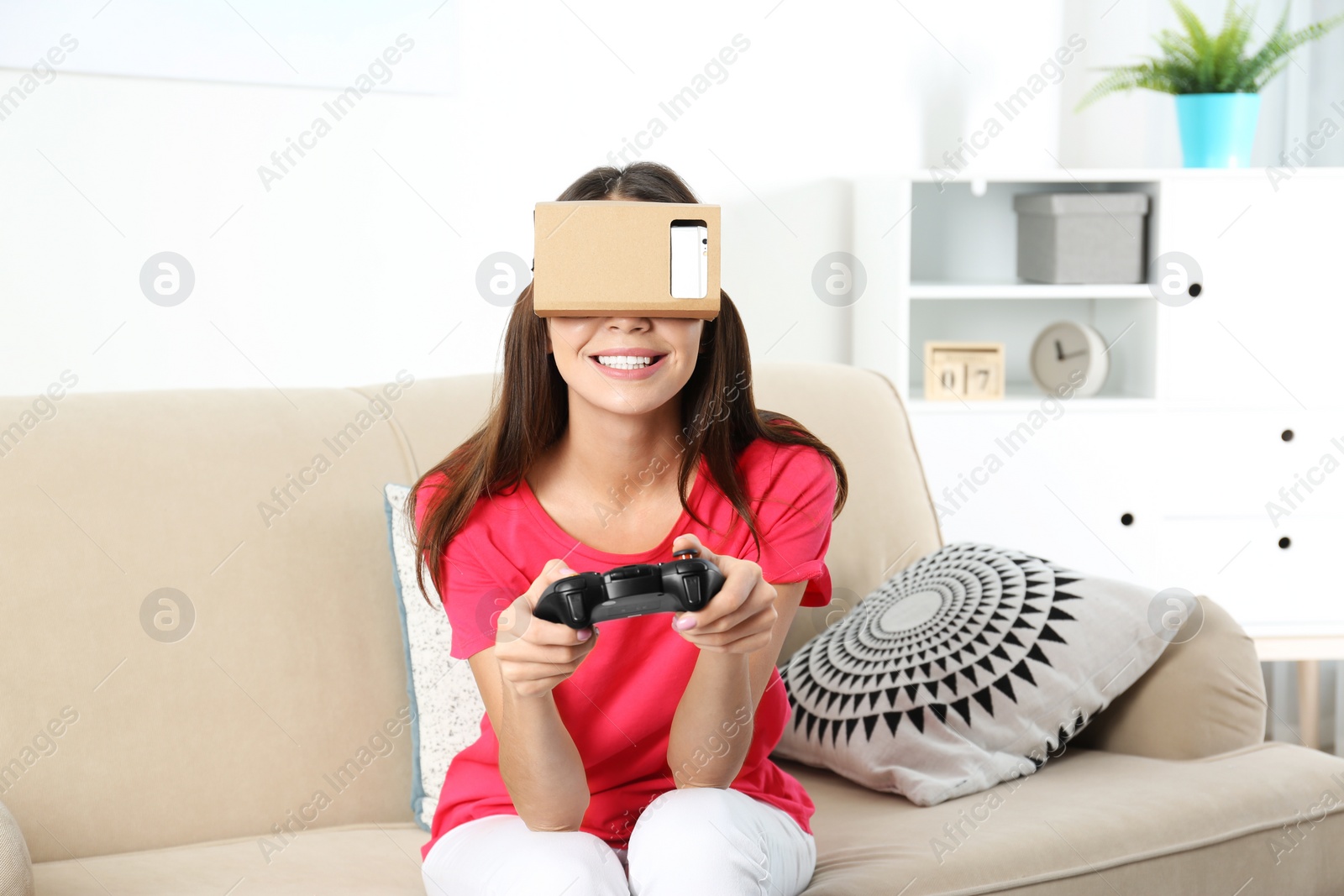 Photo of Young woman using cardboard virtual reality headset at home