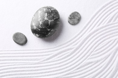 Photo of Zen garden stones on white sand with pattern, flat lay